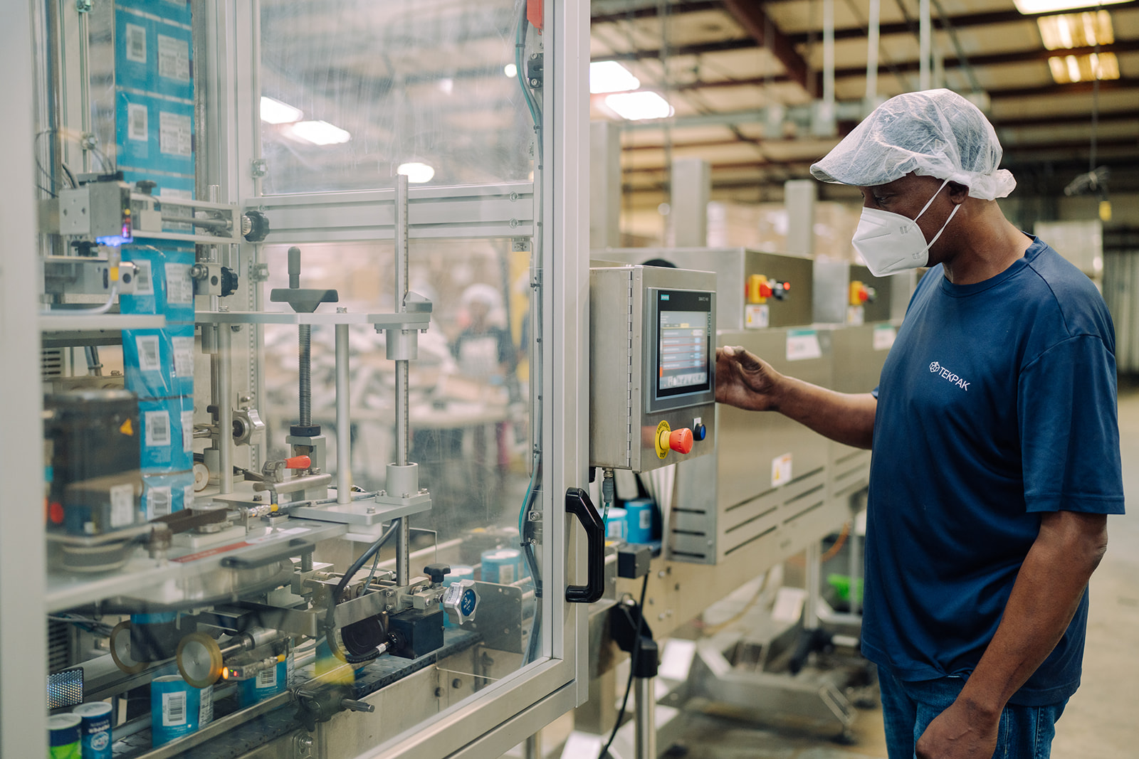 Worker at 2-pack line with glass safety enclosure at TEKPAK's Marion, AL facility